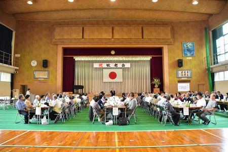 体育館に大勢の参加者達が机を並べて座っている写真