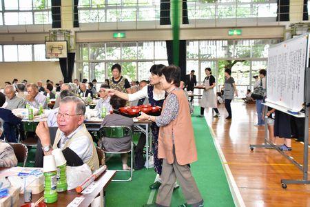 高齢者にお汁お盆に乗せて配っている女性の写真