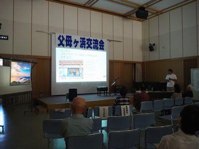 舞台に大きく「父母ケ浜交流会」と書かれた紙があり、その下のスクリーンに映像が映されている写真