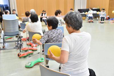 椅子に座っている参加者たちがボールを胸の前で両手で持ち上半身を左にねじっている写真