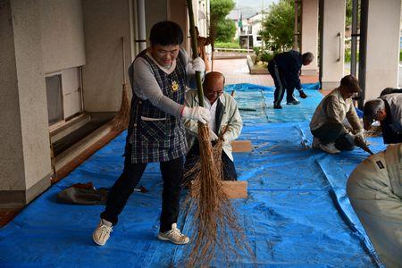 ブルーシートの上で女性が出来上がった竹ぼうきを試しで使っている写真