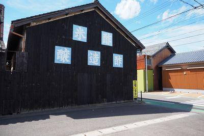 切妻屋根をした建物の黒い壁に白い文字で米酢醸造酢と書かれてある中橋造酢株式会社の外観写真