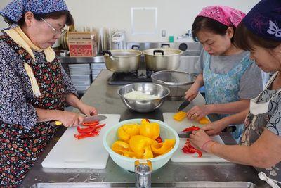赤や黄色のパプリカを包丁で切っている3名の女性の写真