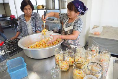 大きなたらいに入れられた刻まれた野菜を瓶に詰めている女性の写真