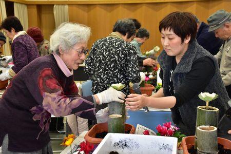 講師の萱原 さつきさんに教わりながら竹に花を入れている白髪の女性の写真