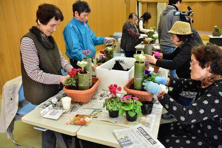 1つの机で4名の参加者達が土の入った竹に花を植えている写真