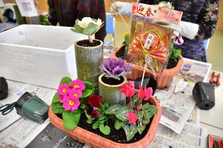 プランターに2本の長短の竹、ピンクや白や紫など5種類の花が飾られており、迎春と書かれた飾りをつけた完成写真を右斜めから撮った写真