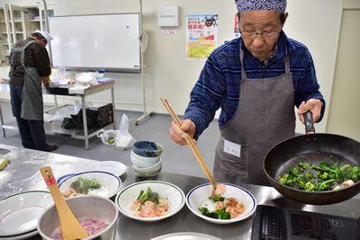 男性がフライパンで調理された食材を皿に盛りつけている写真