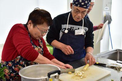 西宇 妙子さんが男性参加者に包丁で野菜の切り方を教えている写真