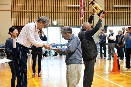 桑山地区の代表の男性が主催者から紙のようなものを受けとっている横で優勝トロフィーを頭上に持ち上げているもう一人の男性の写真