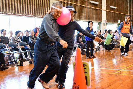 男性2人が肩を組み顔と顔の間にピンクの風船を挟んで走っている写真