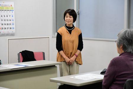 オレンジの服を着た講師の小山 京子さんが教室内の前方に立っている写真