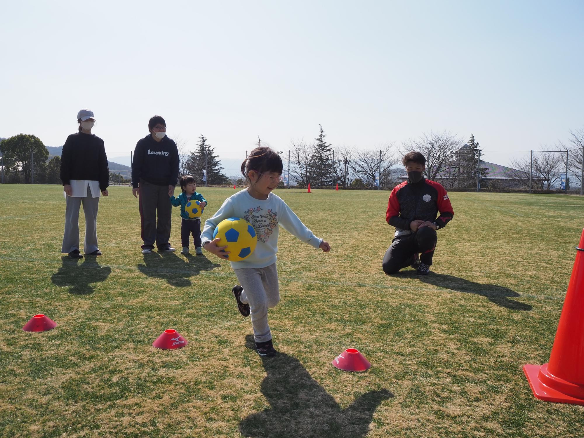 ボールをもって走る子どもと見守るスタッフ