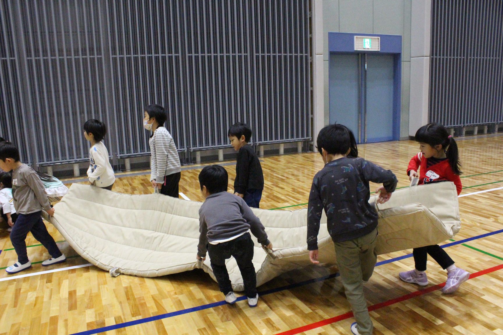 大きなマットを協力して運ぶ子どもたち