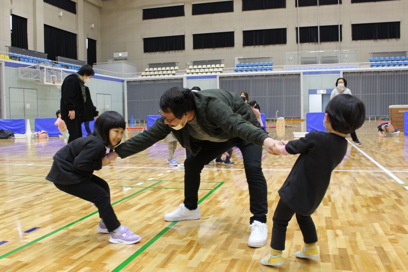 子ども二人と引っ張り合いっこする保護者