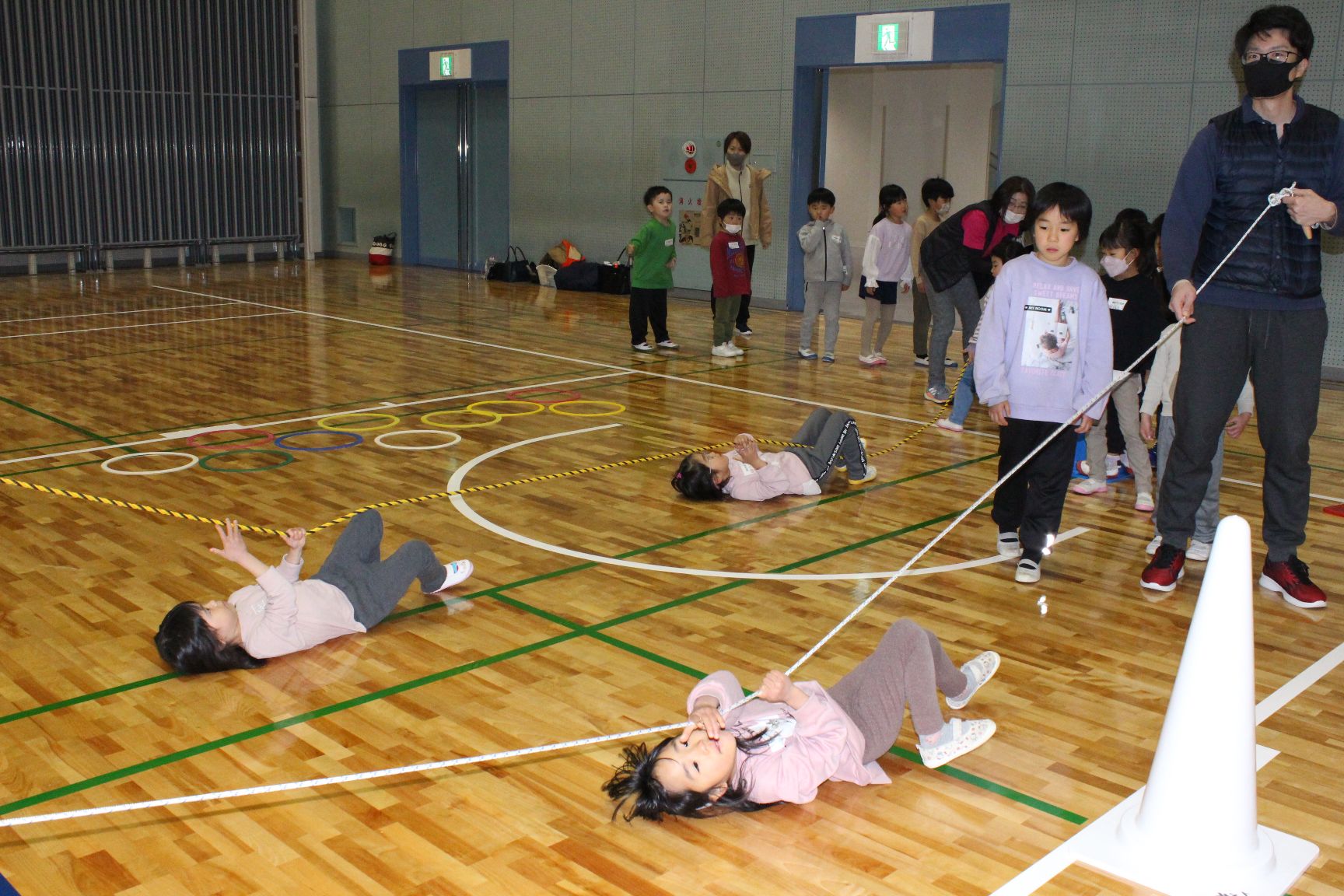あお向けでロープを引っ張る子どもたちとロープを持つ保護者