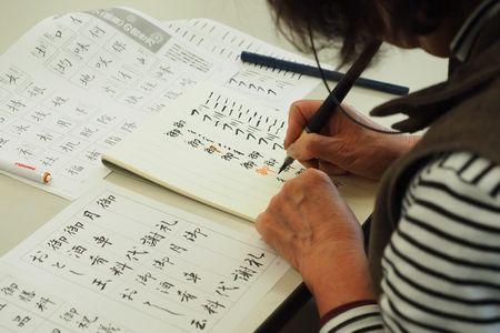 ボーダーの服を着た女性が筆ペンで漢字を書いている手元が写っている写真