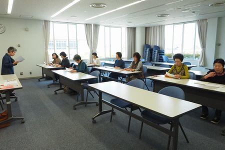 8名の参加者が長テーブルの椅子に座って前に立っている大井 敬子さんの話を聞いている写真