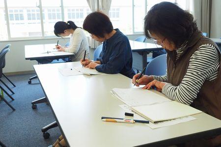 参加者の女性3人が横並びに座っていて、真剣に筆ペンで文字の練習をしている写真