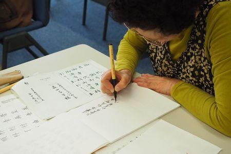 黄色い服を着た女性が筆ペンで文字を書いている手元が写っている写真