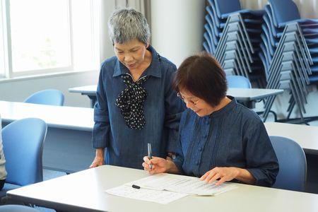 大井 敬子さんが座っている女性の横に立って話しかけている写真