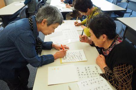 大井 敬子さんが座っている女性の前に立って、紙に書きながら説明をしている写真