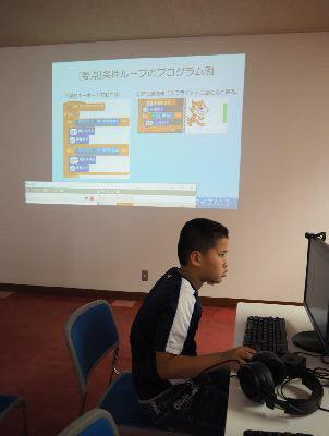 後ろの白い壁がスクリーンのようになって画像が写っている手前で男の子がパソコン操作をしている写真