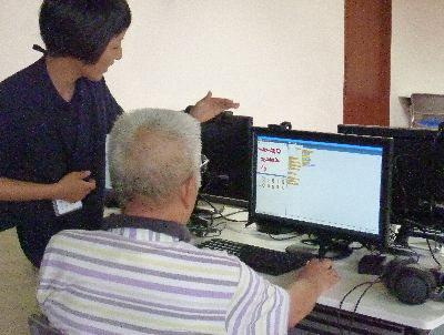 年配の男性が女性の講師に教わりながらパソコンの操作をしている写真