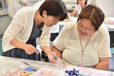 講師の高橋 美貴子さんが右手で持った竹串を左手に持っている瓶の中に入れ受講生に指導をしている写真