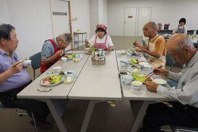 同じテーブルの参加者と話をしながら出来上がった料理を食べている写真