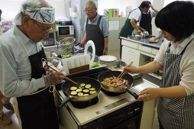 なすを焼いている男性と肉巻きを焼いている女性の写真