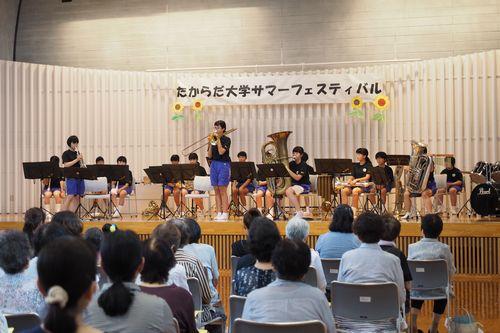 舞台上で演奏を披露している和光中学校吹奏楽部の生徒たちと観客席から見ている来場者の写真