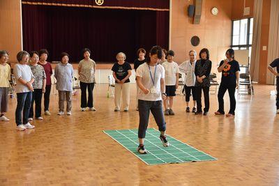 講師の阿河 貴子さんが緑の升目のあるマットの上に立っていて、参加者たちがその周りに集まって見ている写真