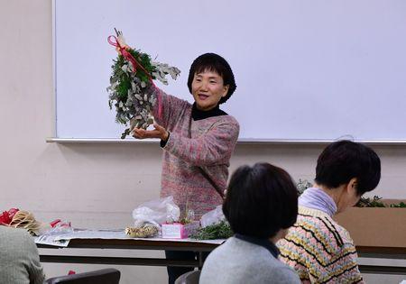 講師の岸上 幸美さんが参加者たちの前に立ってクリスマスリースを見せている写真