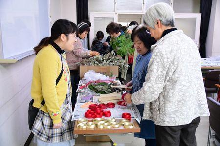 赤と金色のリボンが机の上に置かれていて参加者達がクリスマスリース作りに使うリボンを選んでいる写真