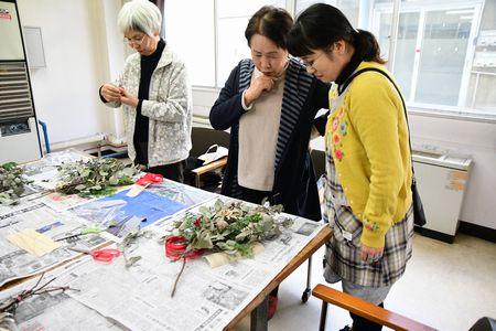 机の上に置いた作成中のクリスマスリースを女性二人が見ている写真