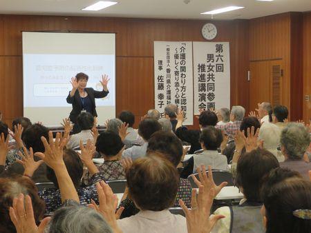 スクリーンの前に講師の佐藤さんが立ち参加者の方を向いて手をパーと広げて、参加者がそれを真似している写真