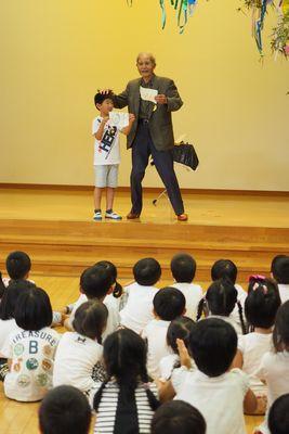 谷口さんと男の子が紙を持って舞台上でマジックをしている写真