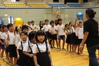 子供達が一列に並び後ろ向きにボールを渡している写真