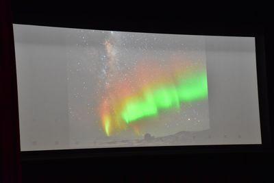 スクリーンに映し出された赤・黄色・緑に光っているオーロラの写真