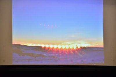 スクリーンに映し出された地平線で光を放っている太陽の写真