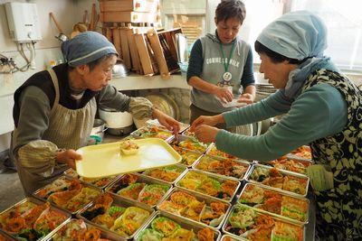 受講生たちが台の上に沢山並べられた弁当箱に調理した食材を詰めている写真