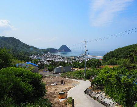 丸山島から見える山道の向こうに住宅地その向こうに海が広がる美しい景色の写真
