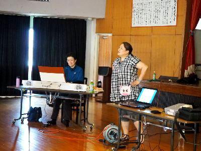 大浦 美樹先生が腰に手を当てて立っている横に、キーボードが置かれており伴奏の片岡 理子先生がキーボードの前に座っている写真