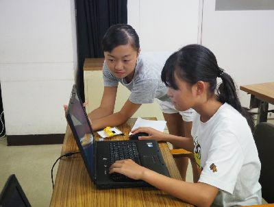 女の子が机でマウスを使いながらパソコンの操作をし、その横で様子を見ている女の子の写真