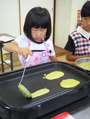 ホットプレートに、お玉でパンケーキの液を、細長く流し入れる女の子の写真