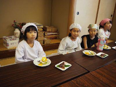 給食着や、エプロンに三角巾をつけて座っている女の子の前に並べられた、高瀬茶パンケーキと水無月の写真