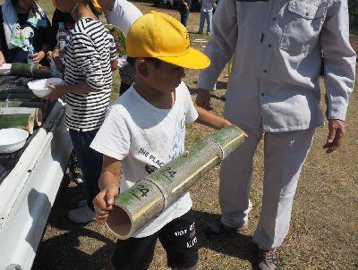 黄色い帽子を被った男子児童が竹筒を運ぼうとしている写真