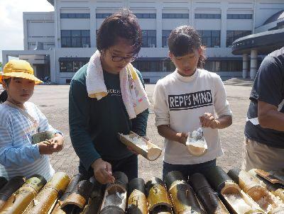 竹筒で炊けたご飯を女子児童が竹の器にスプーンでついでいる写真