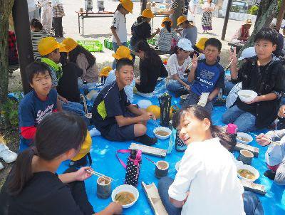 ブルーシートの上に子供たちが座ってご飯と豚汁を食べている写真